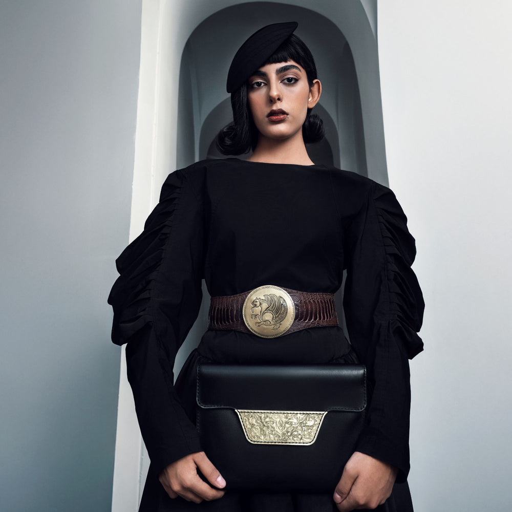 Woman holding a black handbag with decorative elements against a neutral background